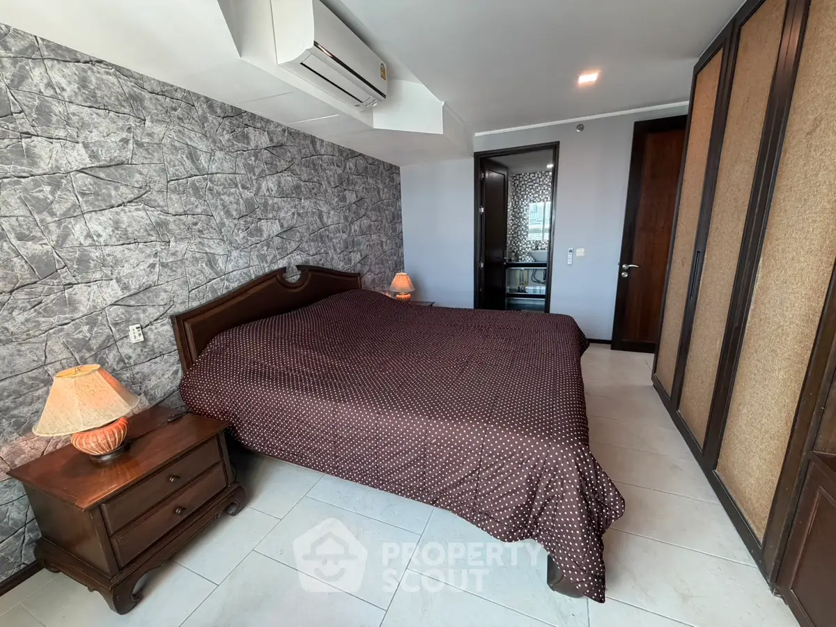 Spacious bedroom with stylish stone accent wall and cozy lighting in modern apartment.