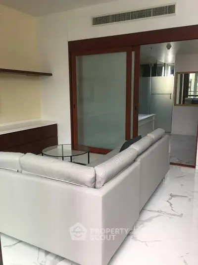Modern living room with sleek white sofa and glass coffee table, featuring elegant marble flooring.