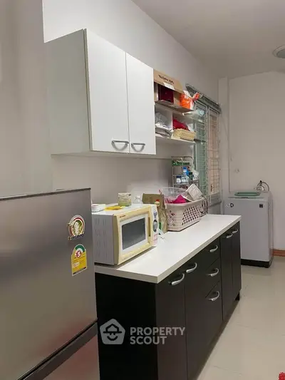 Modern kitchen with sleek cabinets, microwave, and fridge in a cozy apartment setting.