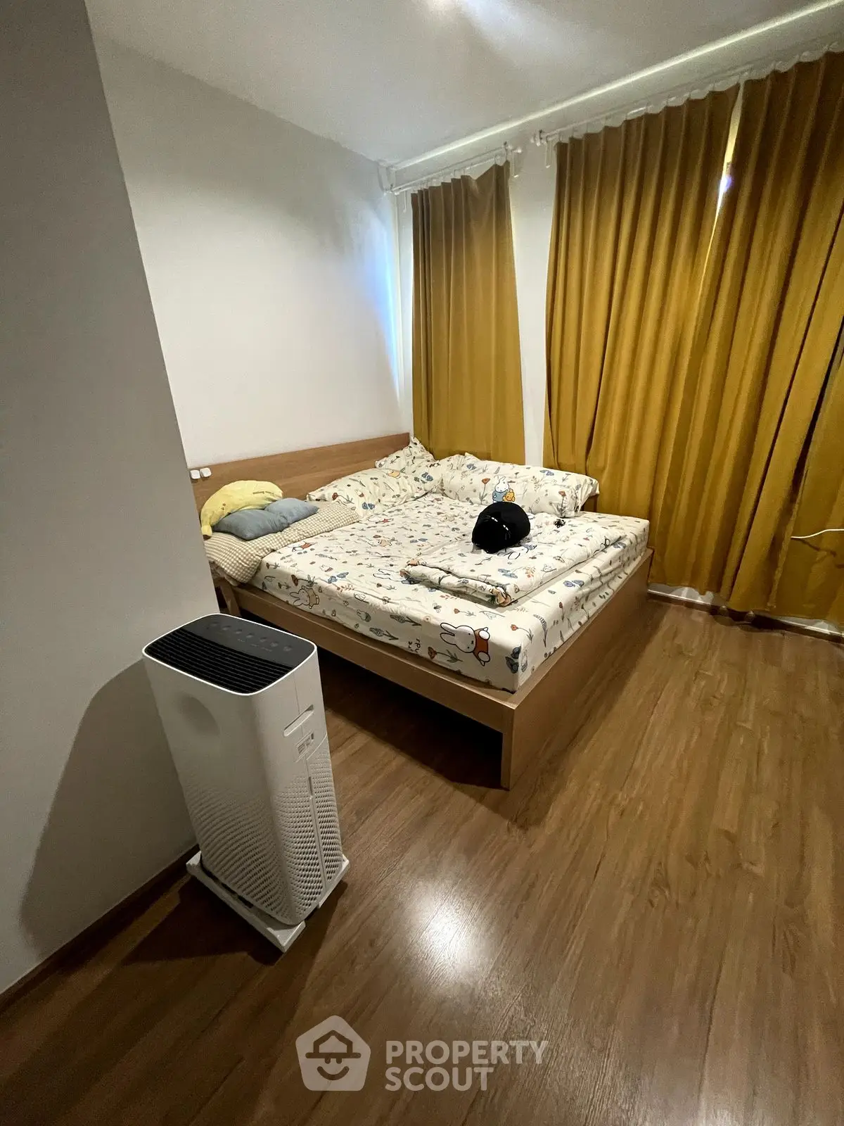 Cozy bedroom with wooden flooring and stylish curtains, featuring a comfortable bed and air purifier.