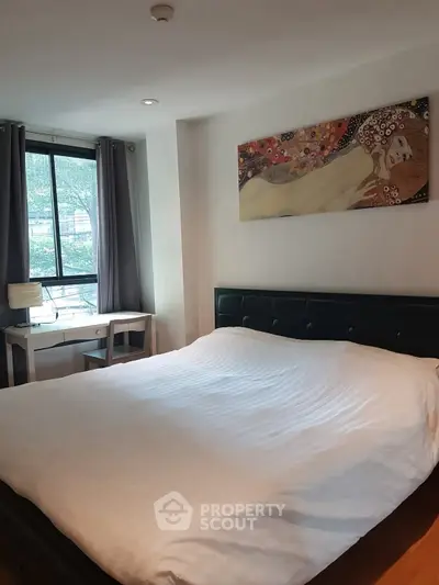 Cozy bedroom with large bed and artistic wall decor, featuring a window view and study desk.