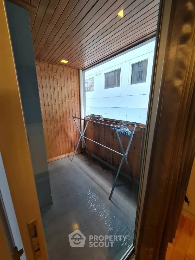 Cozy enclosed balcony with wooden paneling and laundry rack, perfect for urban living.