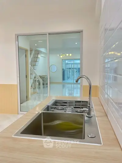 Modern kitchen with sleek sink and open layout, featuring a view of a stylish staircase.