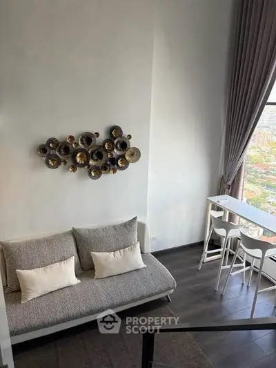 Modern living room with high ceiling and city view, featuring stylish wall art and cozy seating area.