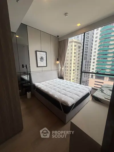 Modern bedroom with large window offering city view, featuring stylish decor and cozy ambiance.