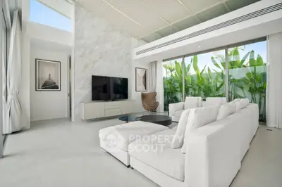 Luxurious modern living room with white sofas, large TV, and floor-to-ceiling windows overlooking lush greenery.