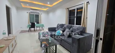 Modern living room with stylish gray sofa and dining area, featuring recessed lighting and large windows.
