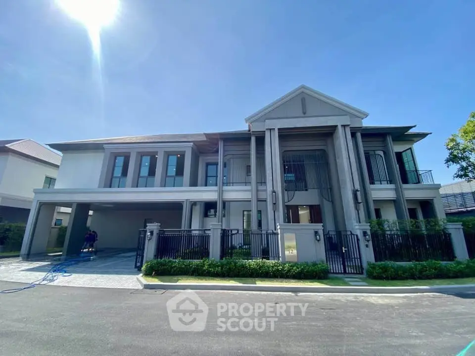 Luxurious modern two-story house with grand entrance and spacious driveway under clear blue sky.