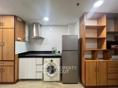 Modern kitchen with wooden cabinets, washing machine, and stainless steel fridge.