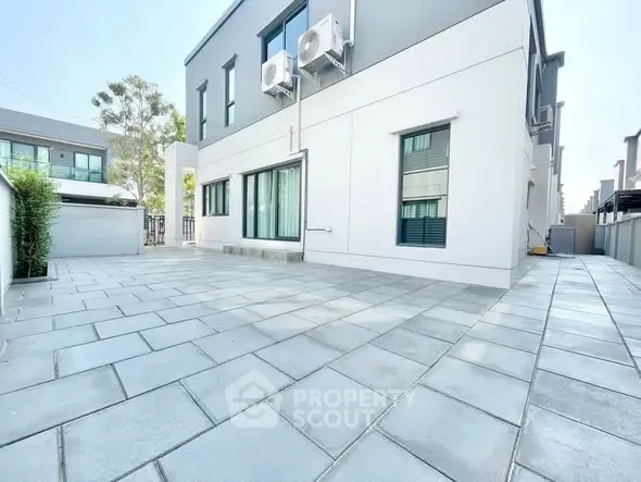 Spacious modern building exterior with large tiled patio and air conditioning units.