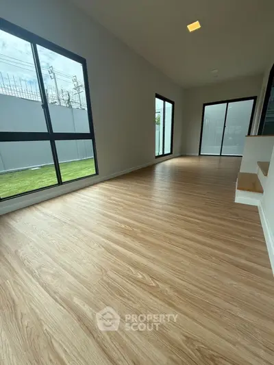 Spacious modern room with large windows and wooden flooring, perfect for natural light lovers.