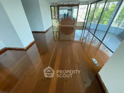 Spacious living room with polished wooden floors and large windows opening to a balcony.