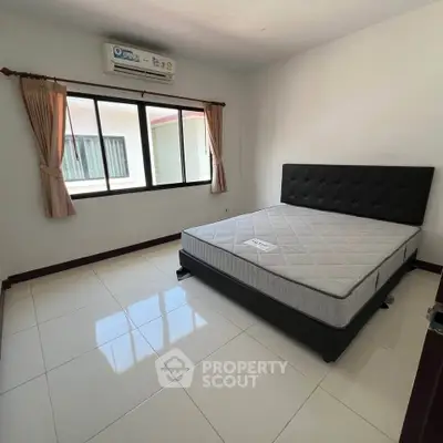 Spacious bedroom with large window and modern bed frame, offering ample natural light and comfort.