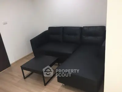 Modern living room with sleek black sofa and minimalist coffee table on wooden flooring.