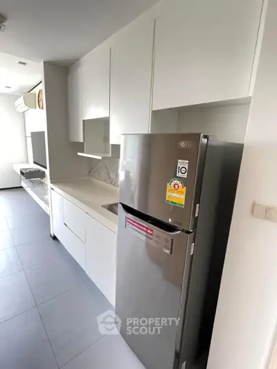 Modern kitchen with sleek white cabinets and stainless steel fridge in a stylish apartment.