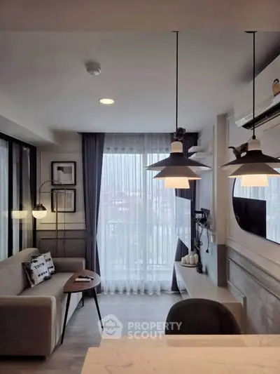Modern living room with stylish lighting and cozy seating area, featuring large windows and elegant decor.