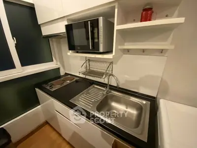 Compact modern kitchen with microwave, electric stove, and sleek cabinetry in urban apartment.