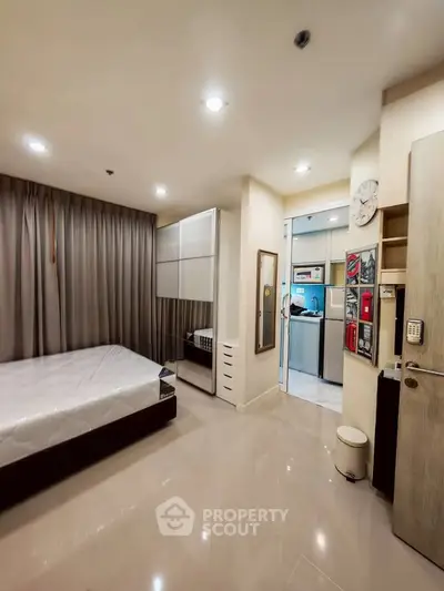 Modern bedroom with sleek design and adjacent kitchen area, featuring neutral tones and ample lighting.