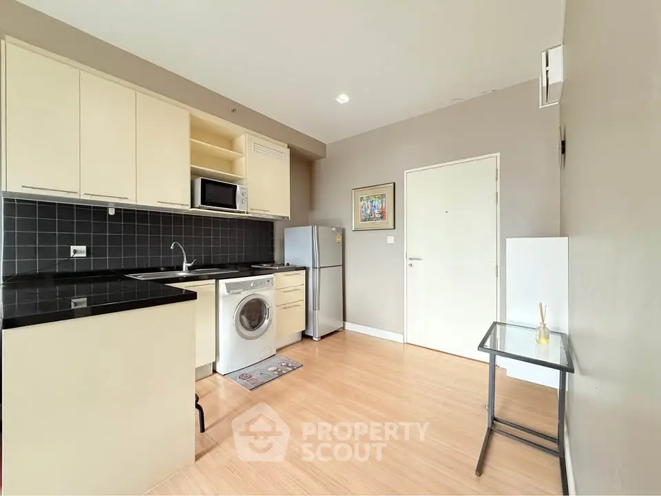 Modern kitchen with sleek black countertops, washing machine, and compact fridge in a cozy apartment.