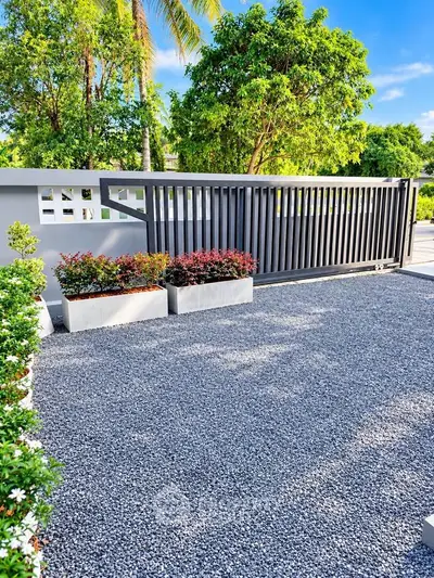 Modern gated entrance with lush greenery and gravel driveway, perfect for a stylish home.