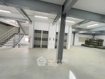 Spacious industrial warehouse with metal beams and stairway access, ideal for storage or commercial use.