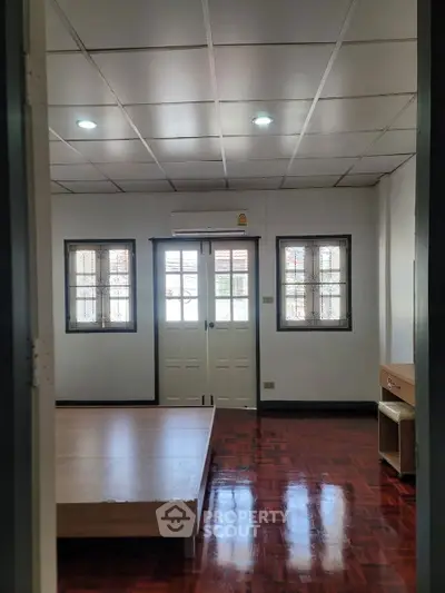 Spacious bedroom with wooden floor and natural light through double windows.