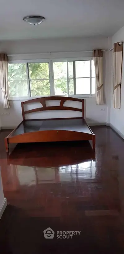 Spacious bedroom with large windows and wooden bed frame, offering serene natural views.