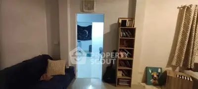 Cozy living room with bookshelf and guitar, leading to a bright adjoining room.