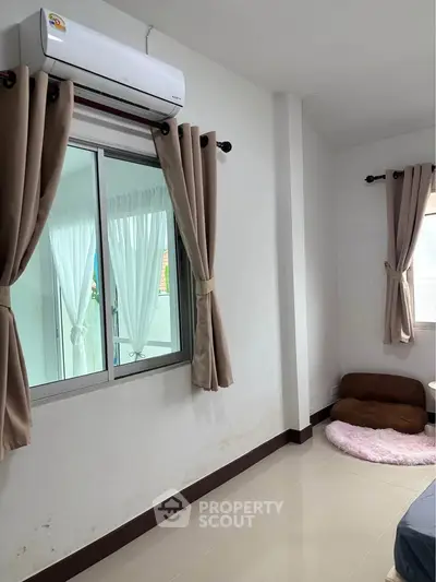 Cozy bedroom with air conditioning and natural light through curtained windows.