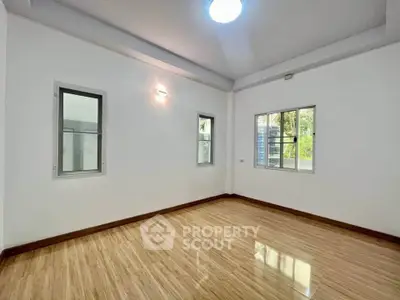 Spacious empty room with wooden flooring and large windows offering natural light.