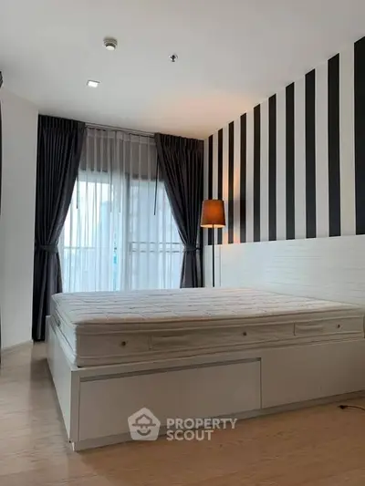 Modern bedroom with striped accent wall and large window, featuring a cozy bed and elegant floor lamp.