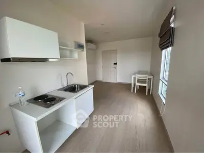 Modern minimalist kitchen with sleek white cabinets and dining area in a bright apartment.