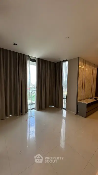 Spacious living room with large windows and elegant curtains in modern apartment.