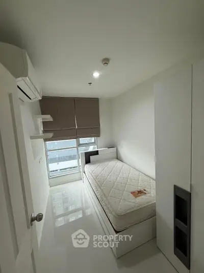 Cozy minimalist bedroom with single bed and modern decor in a high-rise apartment.