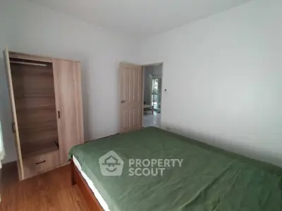 Cozy bedroom with wooden wardrobe and green bedspread, perfect for relaxation.
