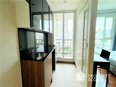 Modern kitchen with sleek black countertops and wooden cabinets, leading to a sunlit balcony with urban views, perfect for city living.