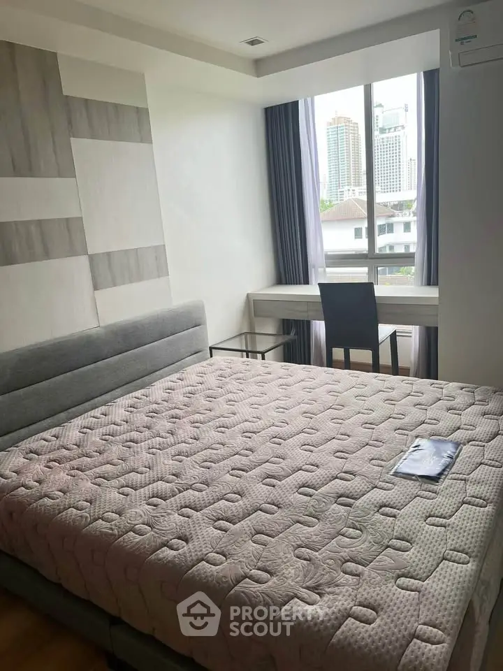 Modern bedroom with large window and city view, featuring a stylish bed and study desk.