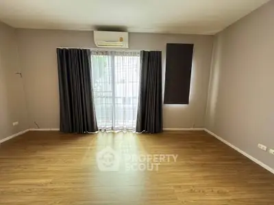 Spacious empty room with wooden flooring and large window, perfect for customization.