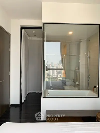 Modern bedroom with glass-enclosed bathtub and city view, offering luxury and comfort.