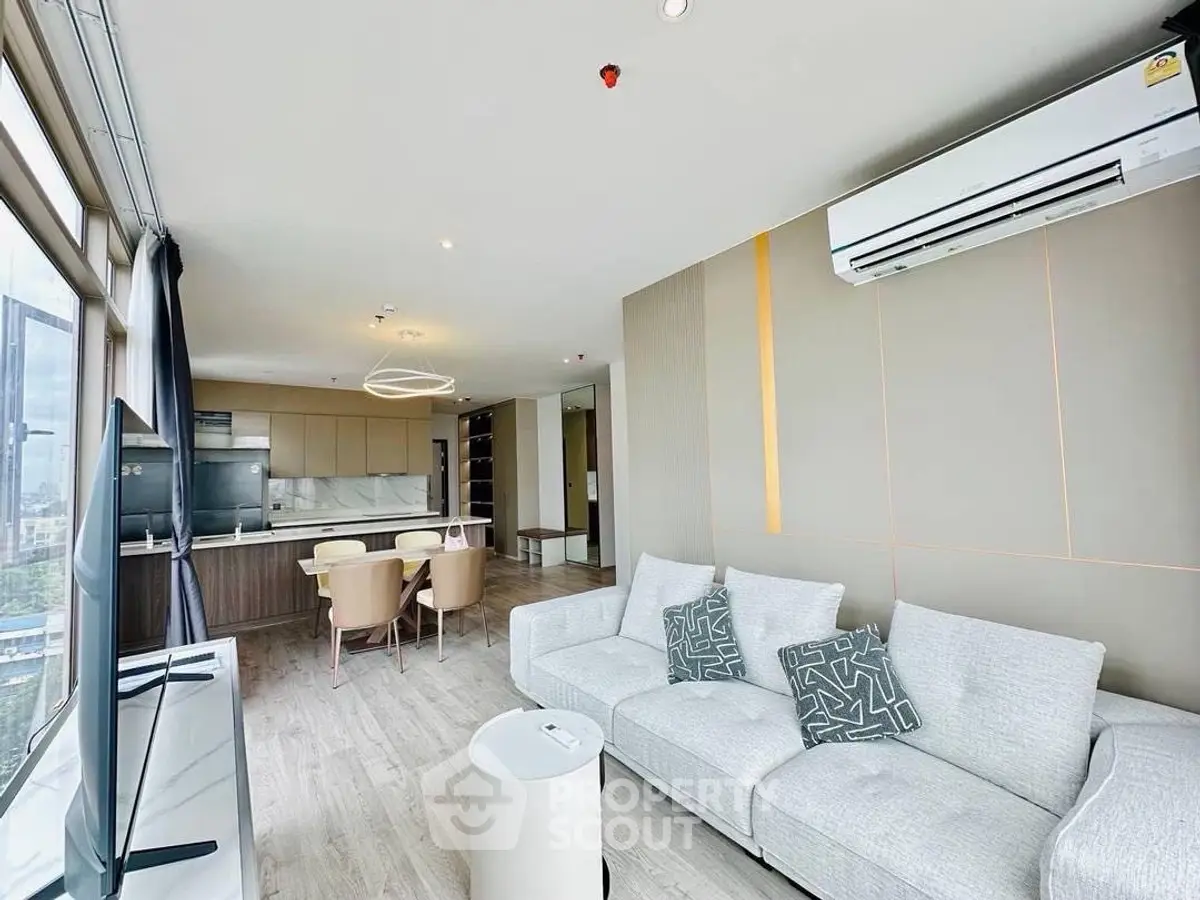 Modern open-plan living room with kitchen, featuring sleek design and large windows.