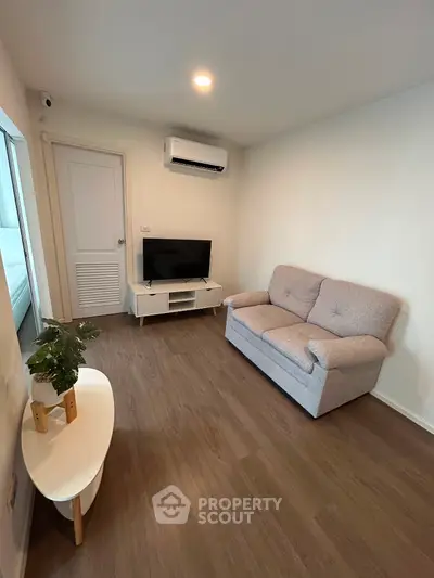 Cozy living room with modern sofa and TV, featuring sleek wooden flooring and minimalist decor.