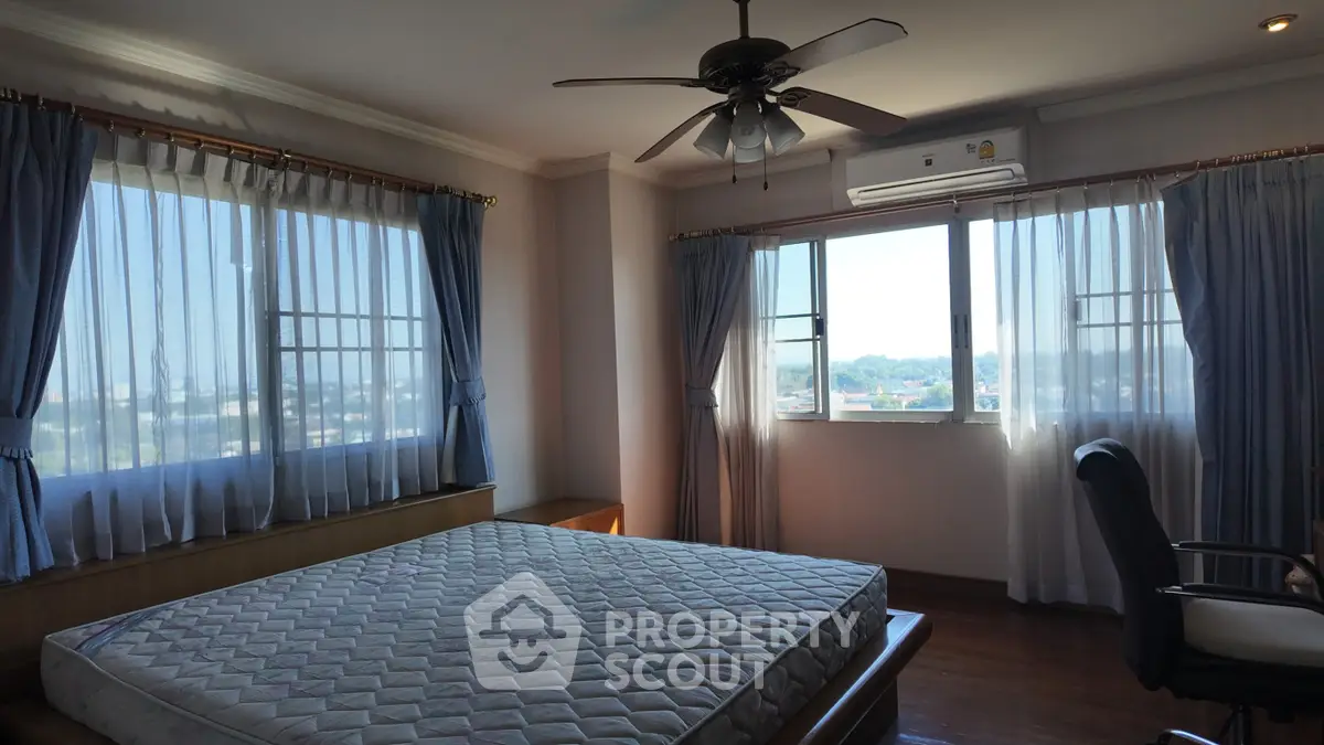 Spacious bedroom with large windows and ceiling fan, offering a serene view.