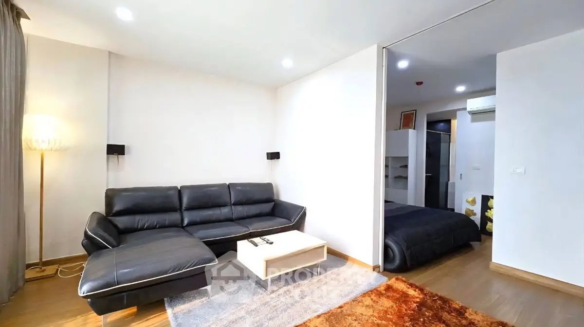 Modern living room with sleek black leather sofa and cozy bedroom view