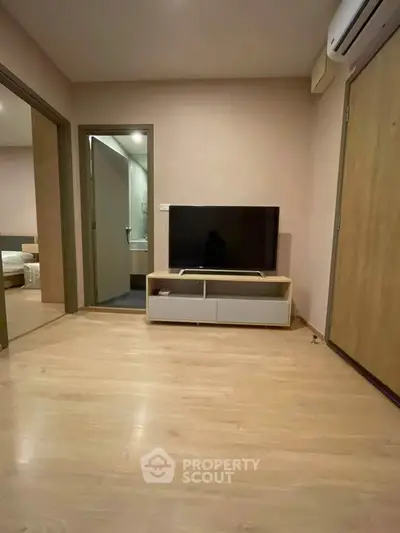 Modern living room with wooden flooring and sleek TV setup, adjacent to a cozy bedroom.