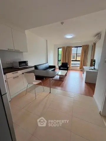 Modern open-plan living room with kitchen, featuring sleek furniture and large windows for natural light.