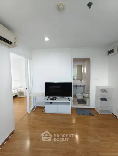 Modern apartment interior with TV, wooden floors, and bathroom access.