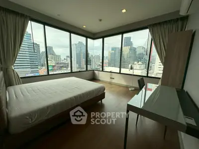 Spacious bedroom with panoramic city views and modern furnishings in a high-rise apartment.