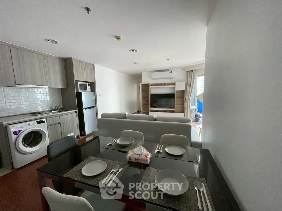 Modern open-plan living room with kitchen, dining area, and laundry appliances in a stylish apartment.