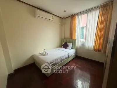 Cozy bedroom with single bed and air conditioning, featuring wooden flooring and natural light from large window.
