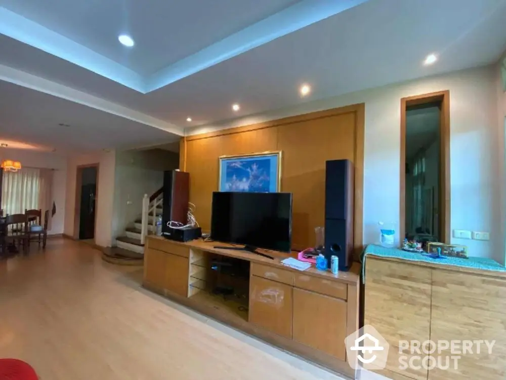 Spacious living room with polished wooden cabinetry and modern entertainment system, elegant lighting, and warm wooden flooring.